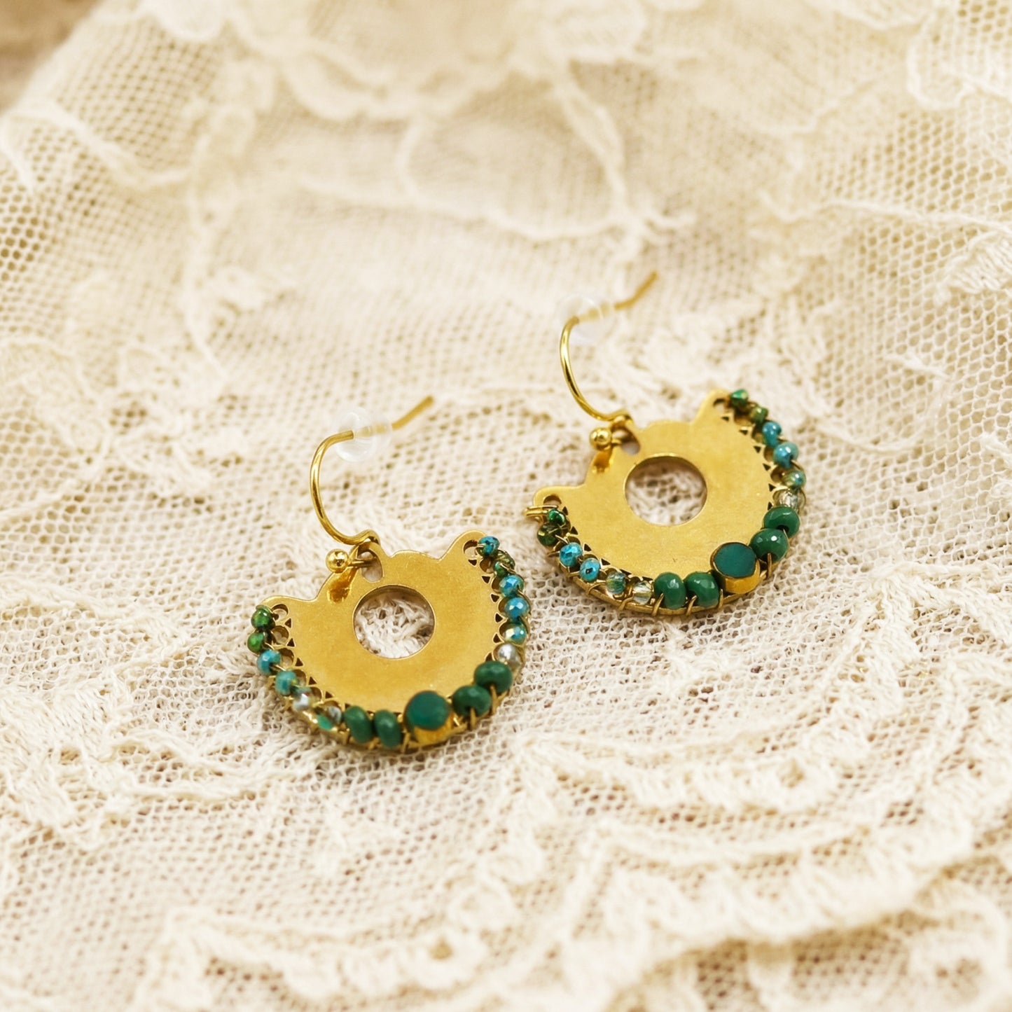 Gold earrings with green gemstones on a lace background