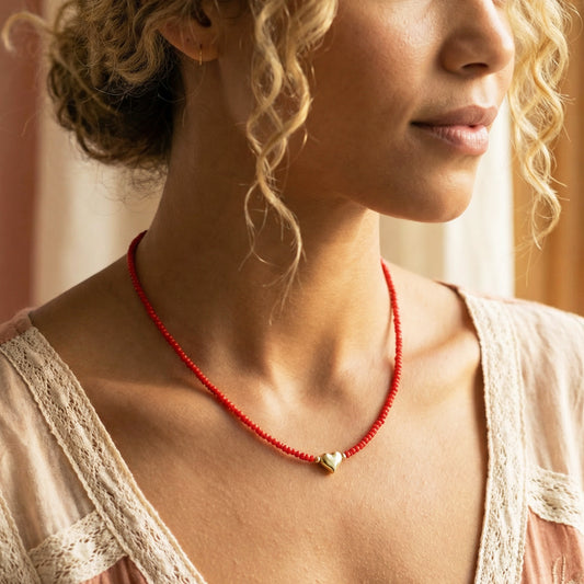Woman wearing a red beaded necklace with a heart pendant.