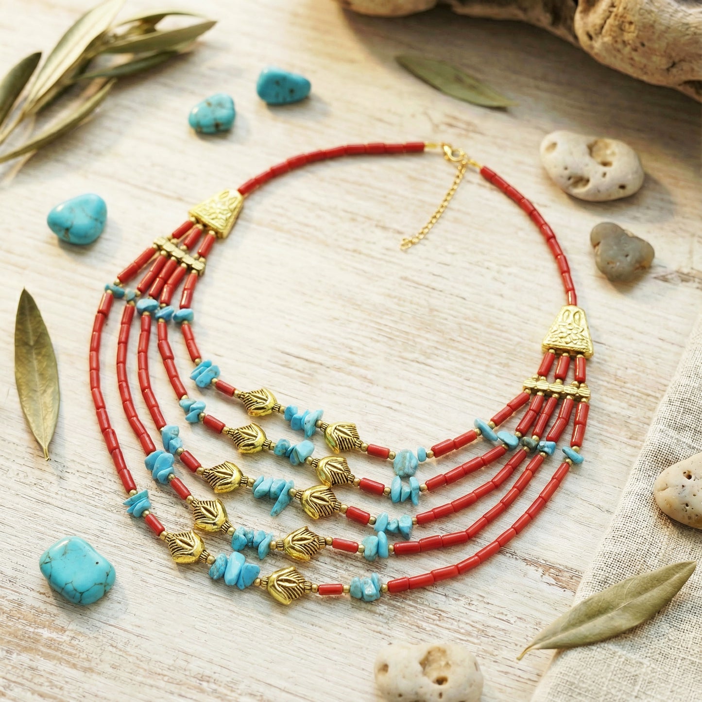 Necklace with red and blue beads on a wooden surface with leaves and stones.