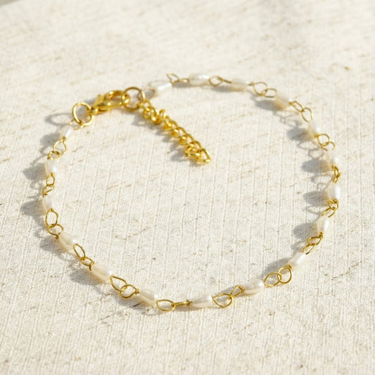 Gold anklet with white beads on a beige fabric background