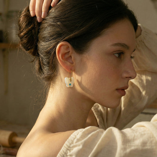 Woman with a bun and earrings, wearing a beige garment, in a warm-toned setting.