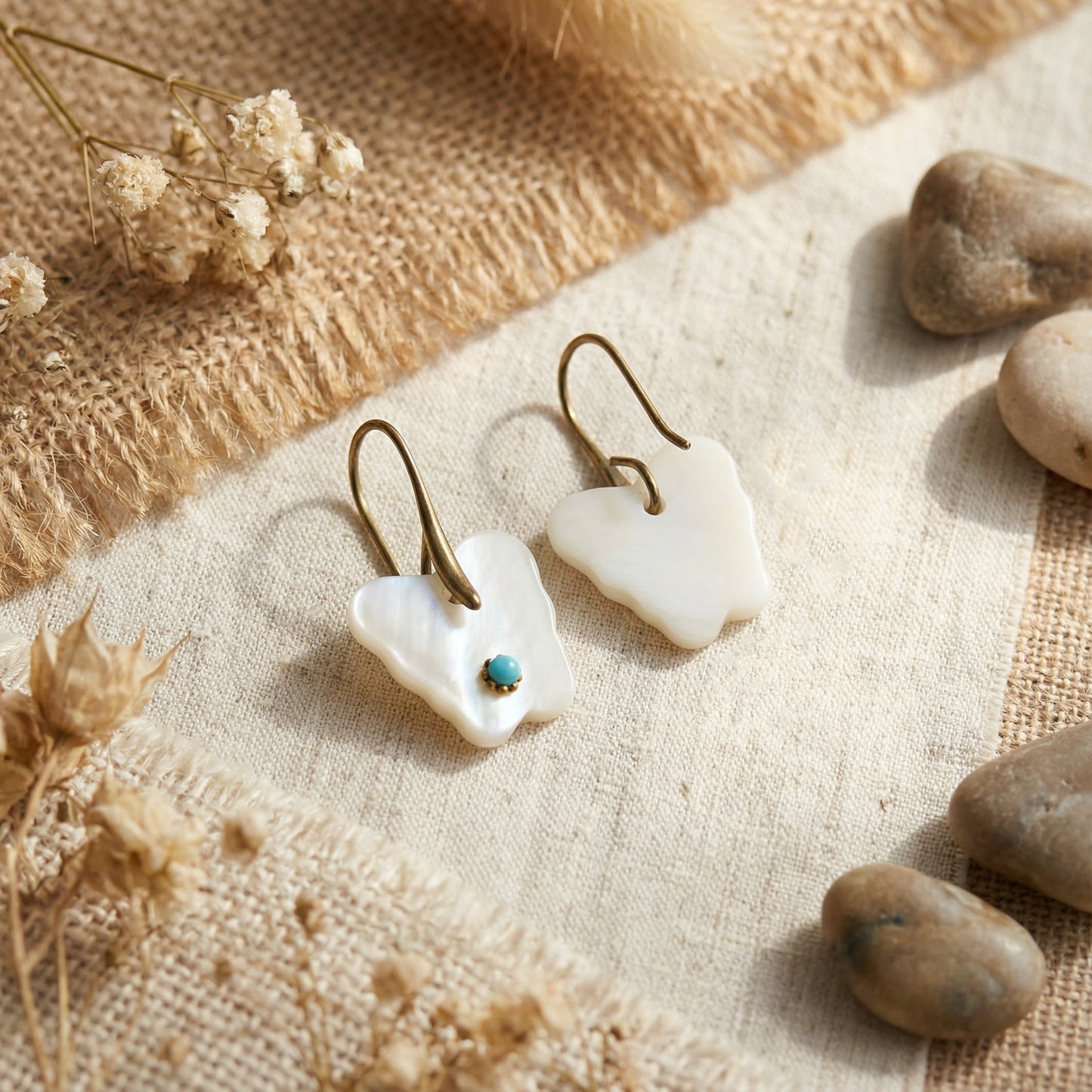 Pair of white earrings with a turquoise stone on a textured surface with stones and dried flowers.