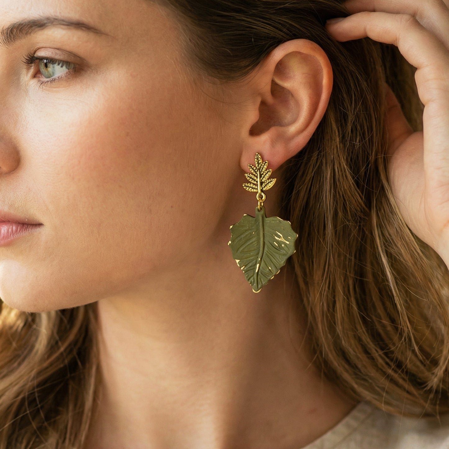 Close-up of a woman wearing leaf-shaped earrings with gold and green leaves.
