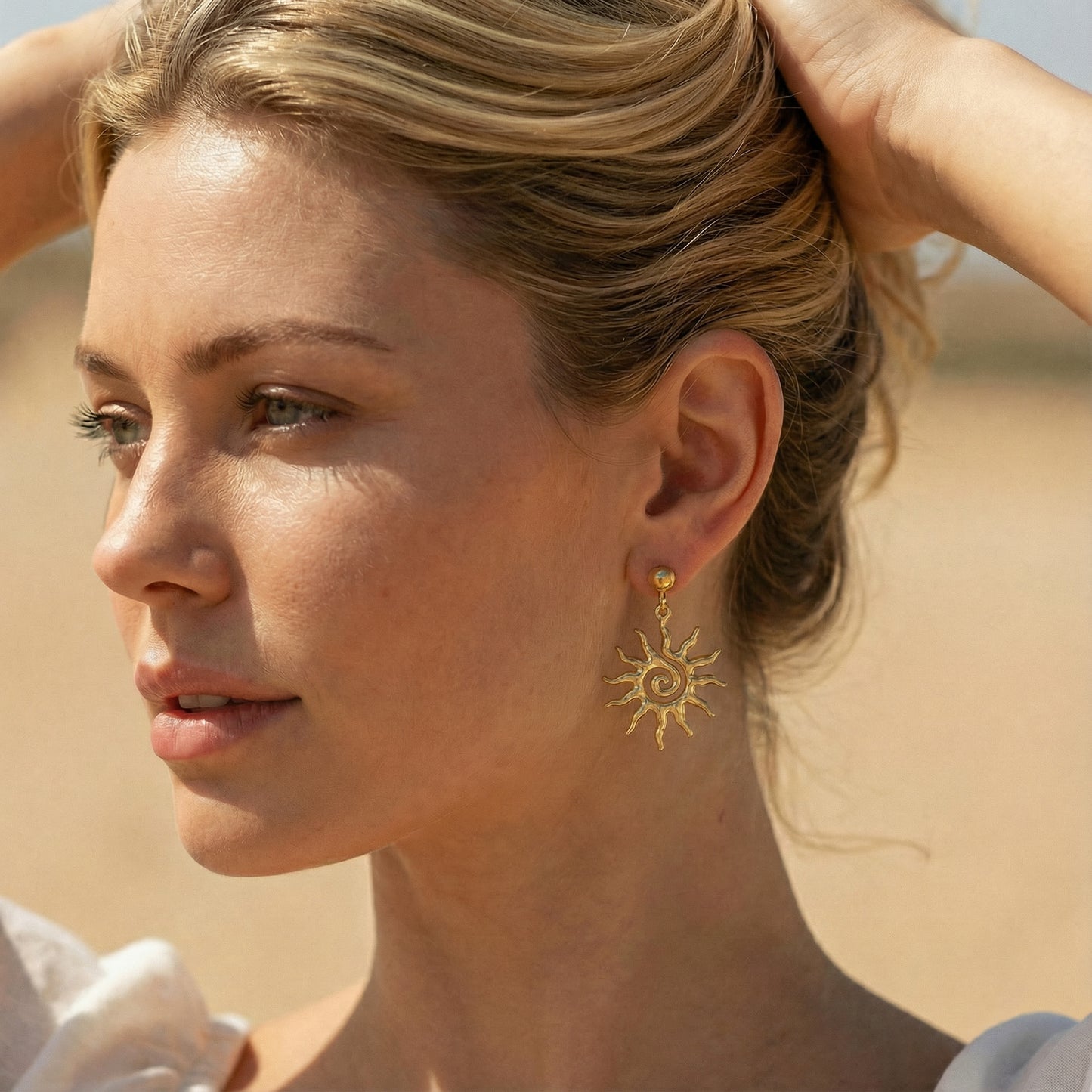 Woman wearing gold sun-shaped earrings against a desert background
