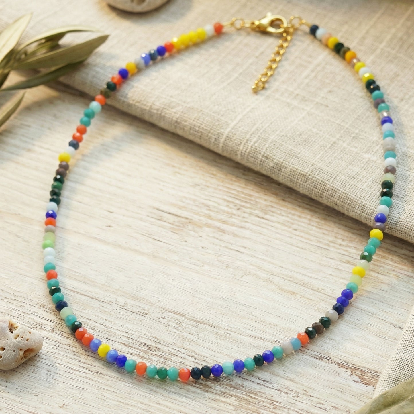 Colorful beaded necklace on a textured surface with leaves and fabric