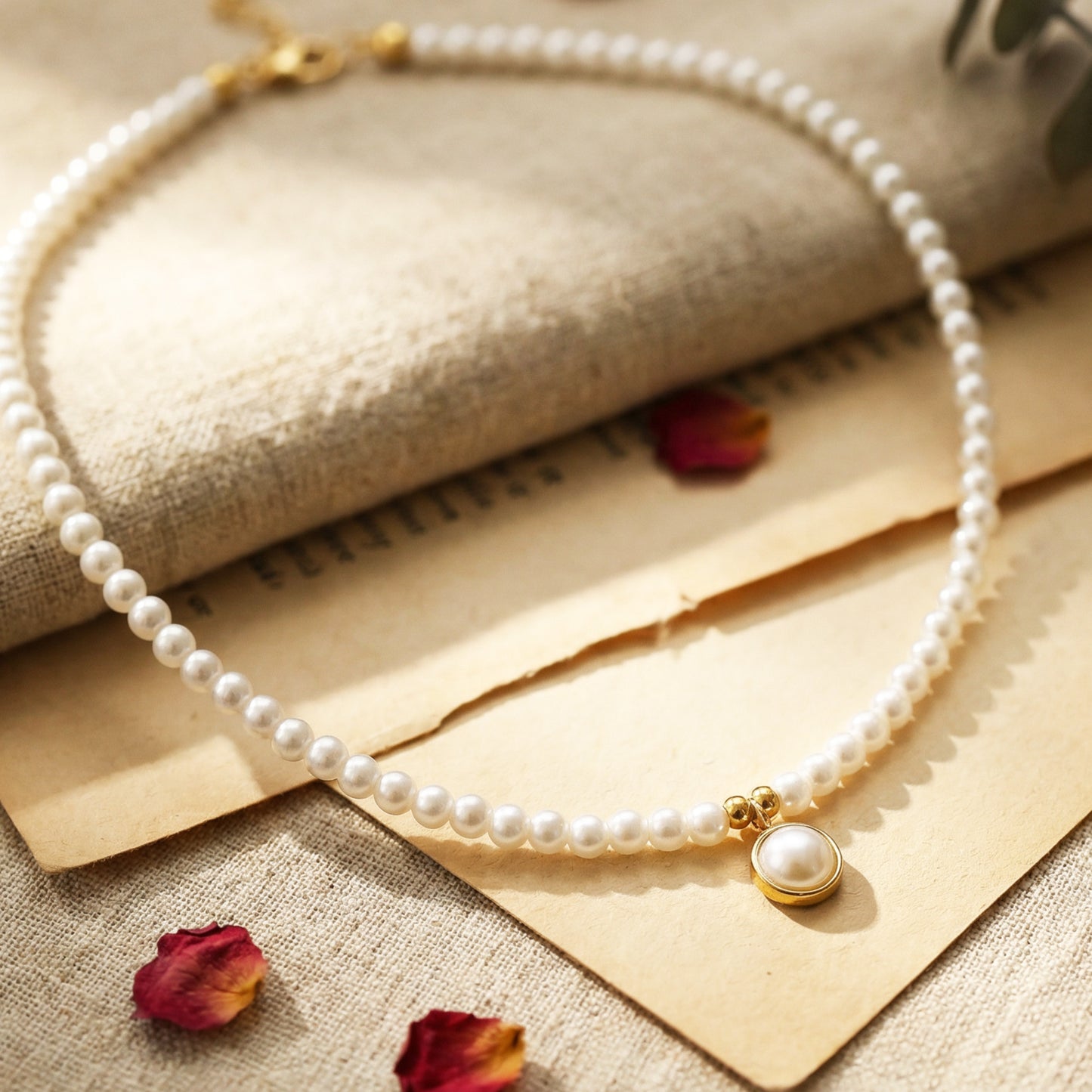 Pearl necklace with a gold clasp on a textured surface with dried flowers.