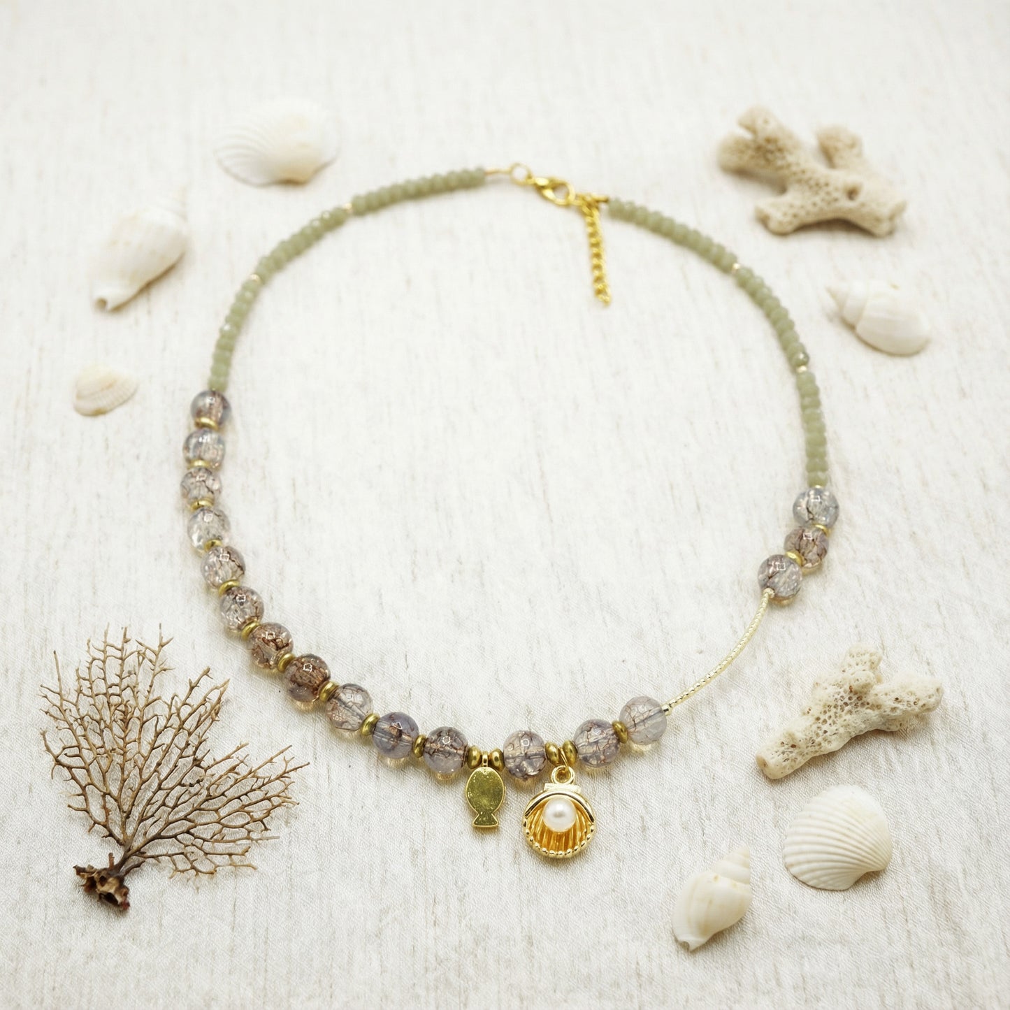 Necklace with shell charm on a sandy background with shells and coral