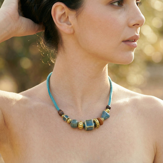 Woman wearing a blue beaded necklace with a blurred natural background