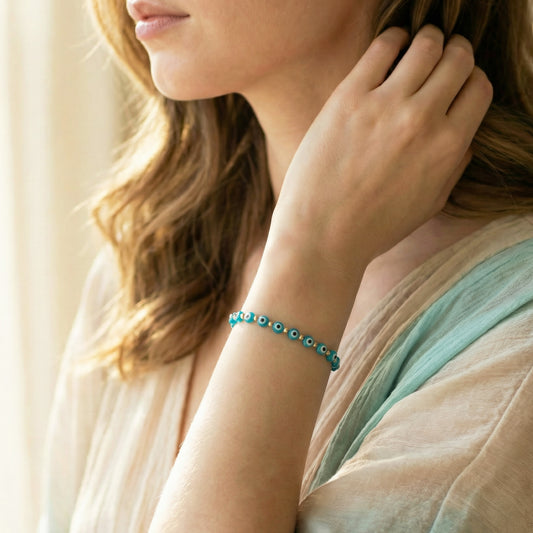 Woman wearing a turquoise bracelet with small beads, adjusting her hair.