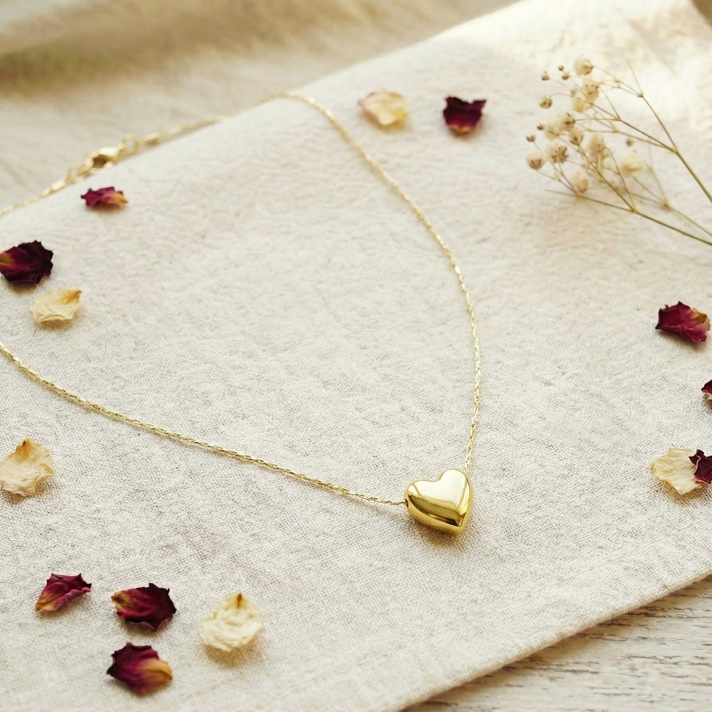 Gold heart-shaped necklace on a textured surface with dried flowers