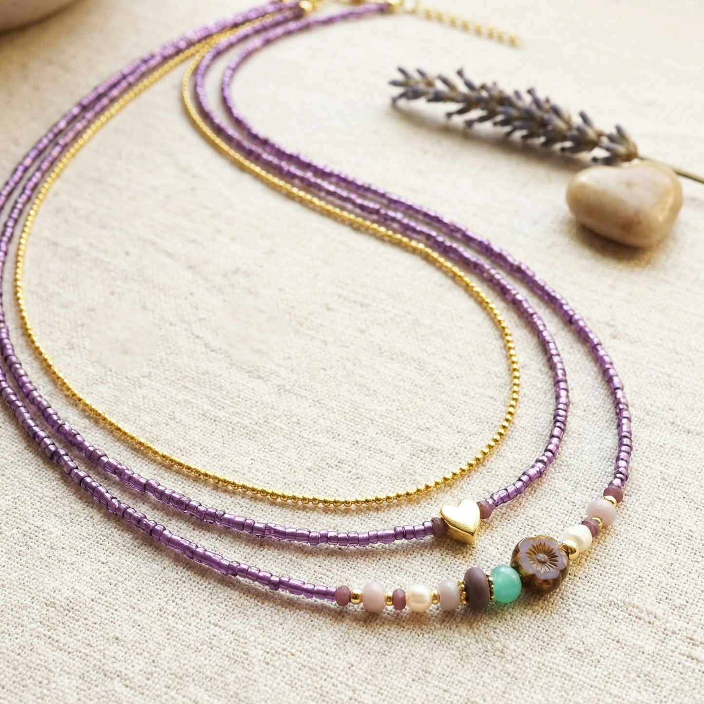 Two beaded necklaces on a textured surface with a stone and lavender sprig.