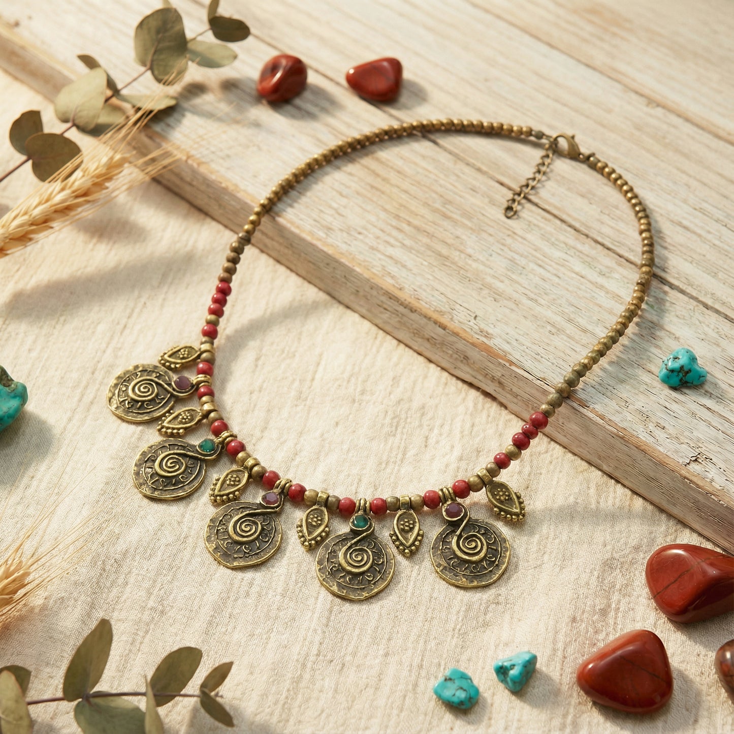 Decorative necklace with beads and pendants on a wooden surface with stones and leaves.