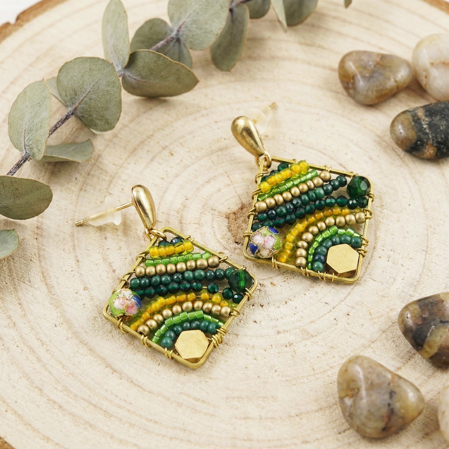 Pair of beaded earrings on a wooden surface with green leaves and stones.