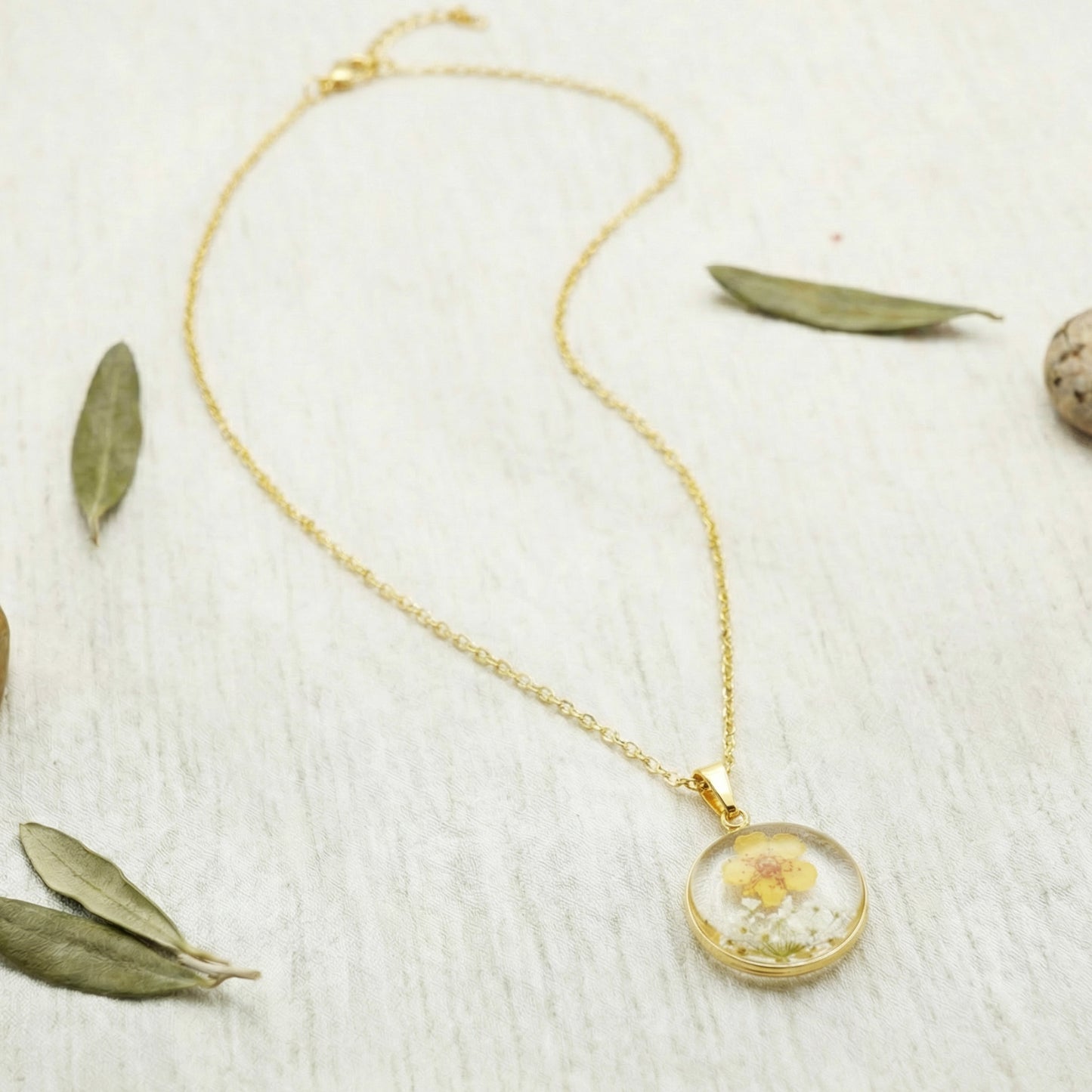Gold necklace with a round pendant featuring a dried flower on a light wooden surface.