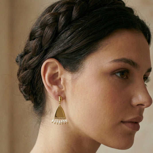 Woman wearing gold earrings with a braided hairstyle against a neutral background