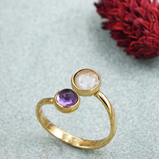 Gold ring with two gemstones on a textured surface