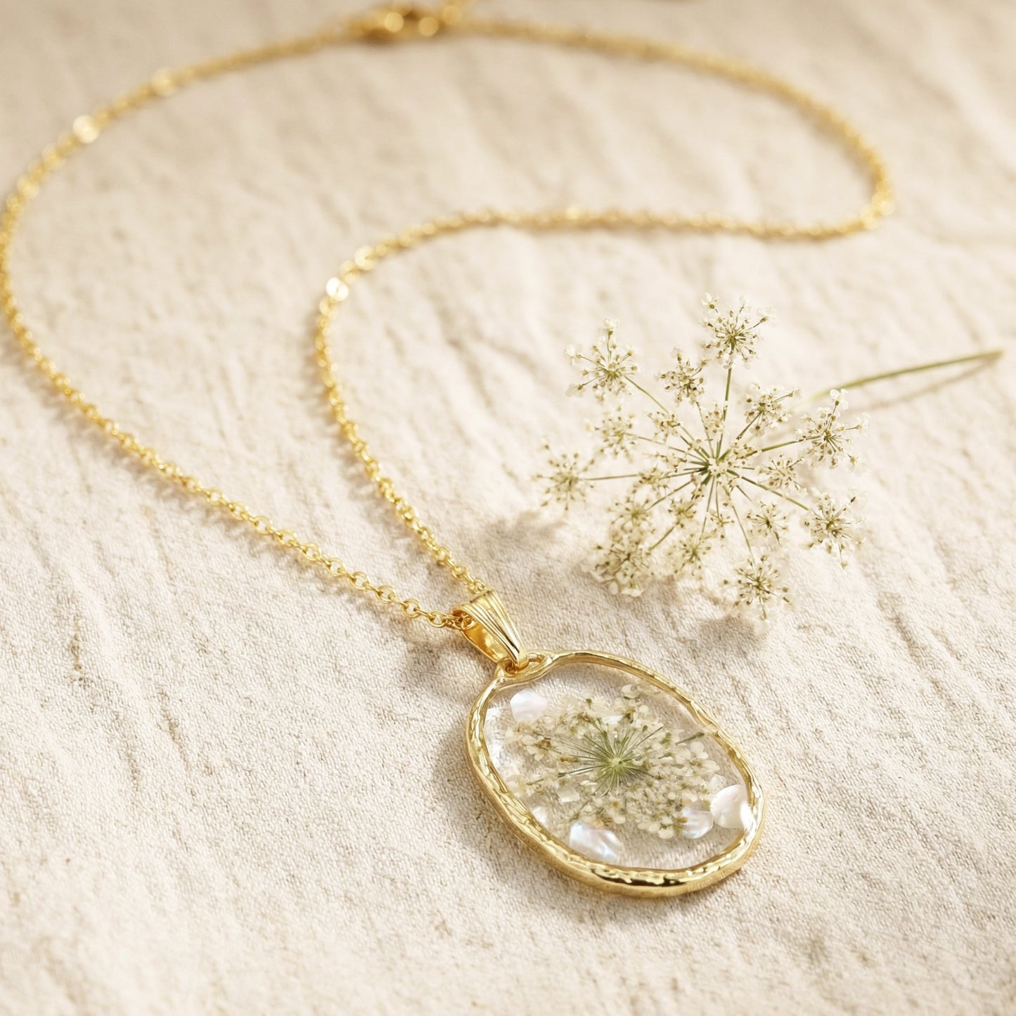 Gold necklace with a clear pendant featuring pressed flowers on a light background