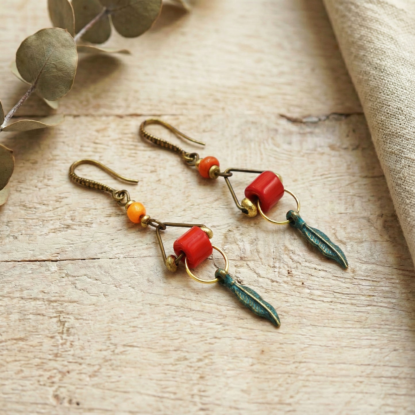 Pair of earrings with red and green beads on a wooden surface