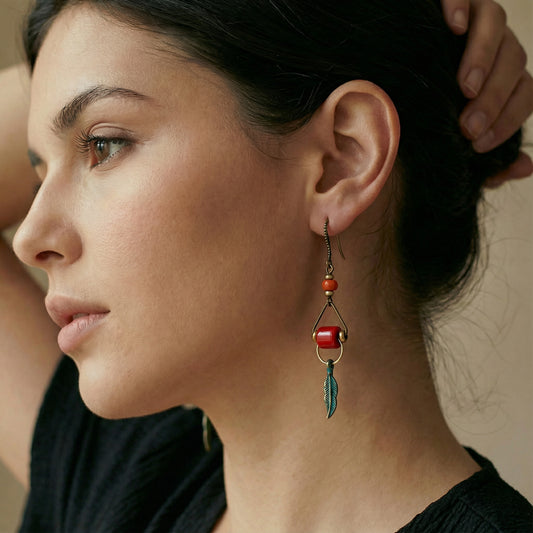 Close-up of a woman wearing an earring with red beads and a green feather.