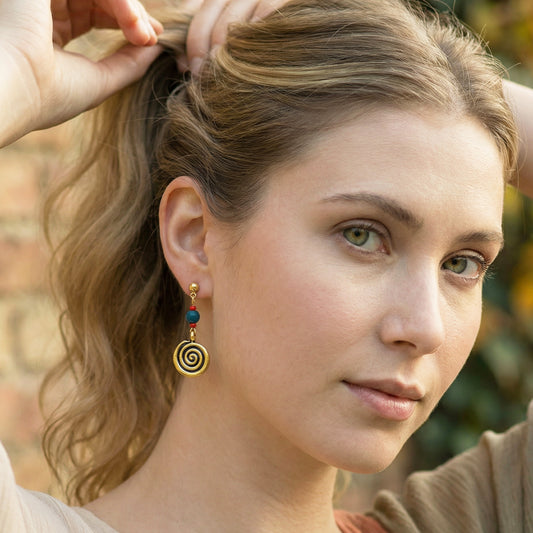 Close-up of a woman wearing spiral earrings with a blurred outdoor background