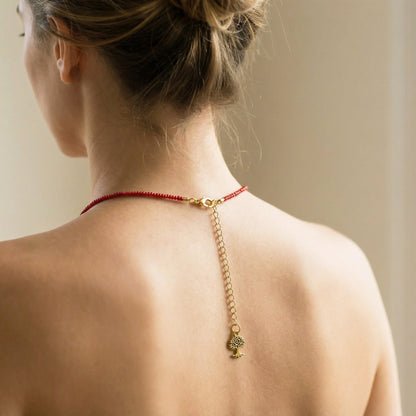 Woman wearing a red necklace with a gold chain and pendant on a neutral background
