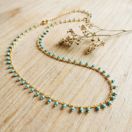 Gold necklace with turquoise beads on a wooden surface