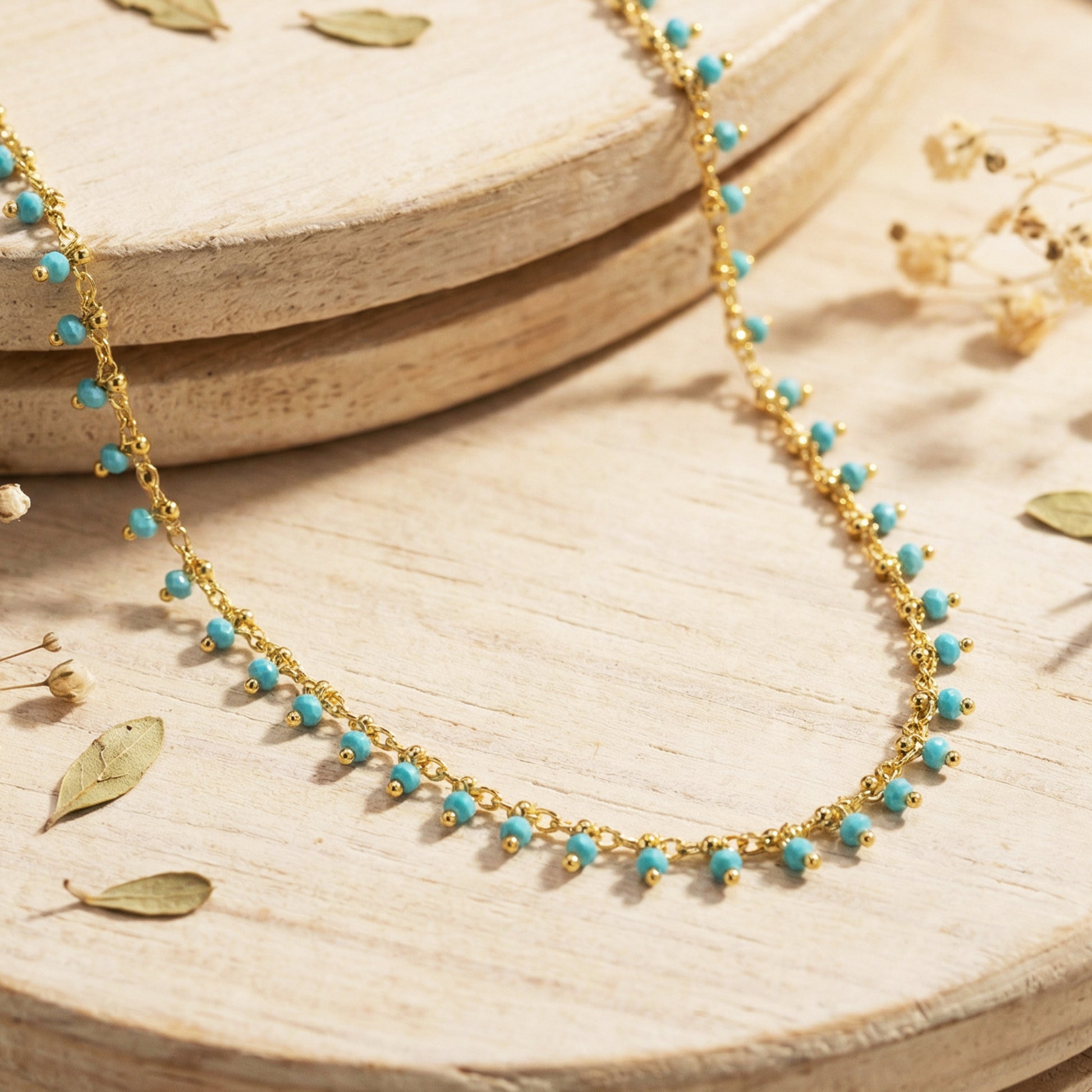Gold necklace with turquoise beads on a wooden surface with dried leaves