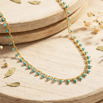 Gold necklace with turquoise beads on a wooden surface with dried leaves