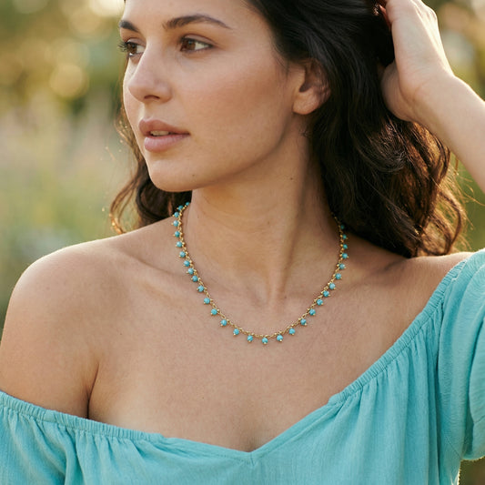 Woman wearing a turquoise off-shoulder top and necklace with a blurred natural background