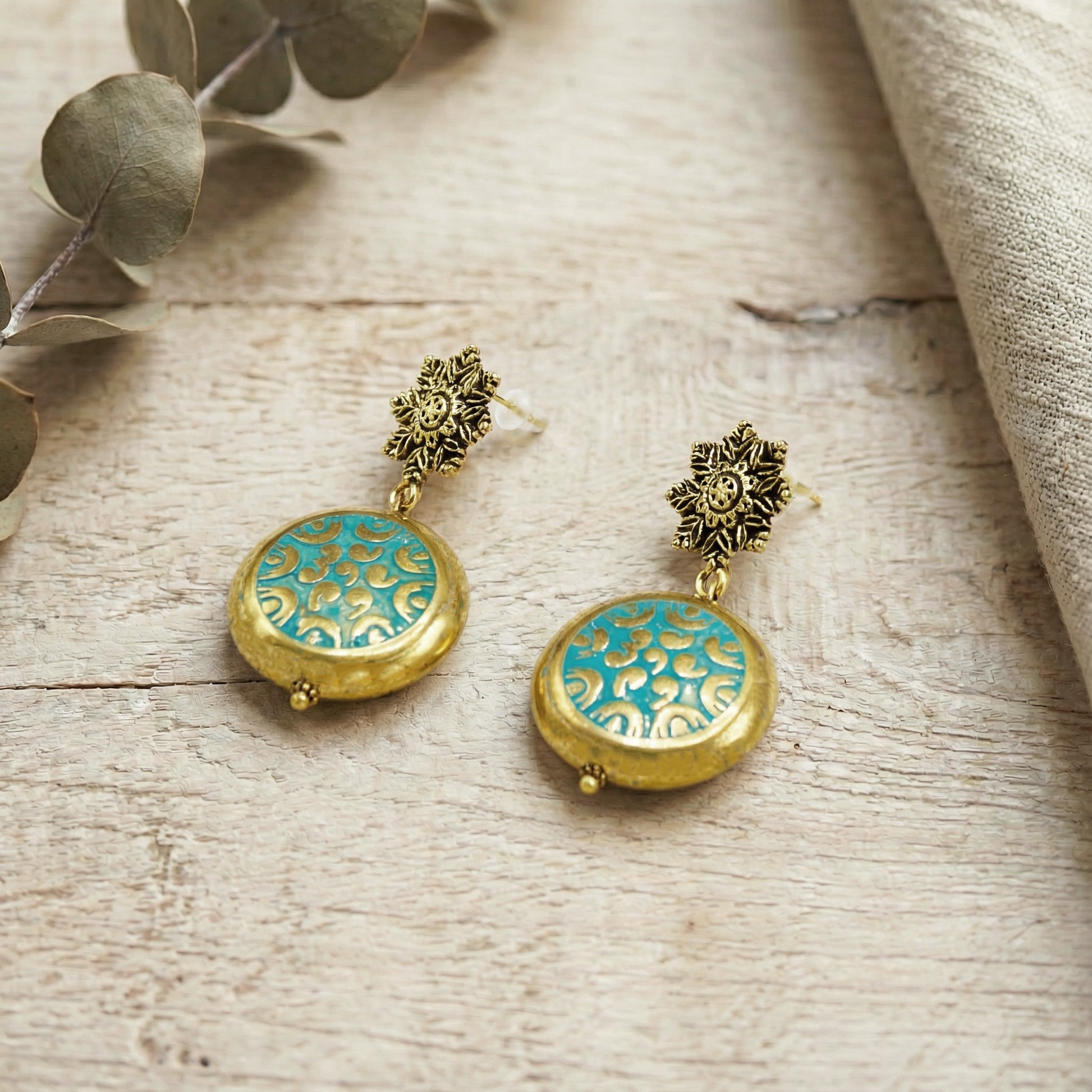 Gold and turquoise earrings on a wooden surface with leaves.