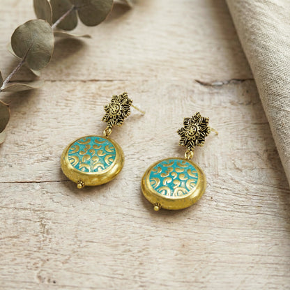 Gold and turquoise earrings on a wooden surface with leaves.