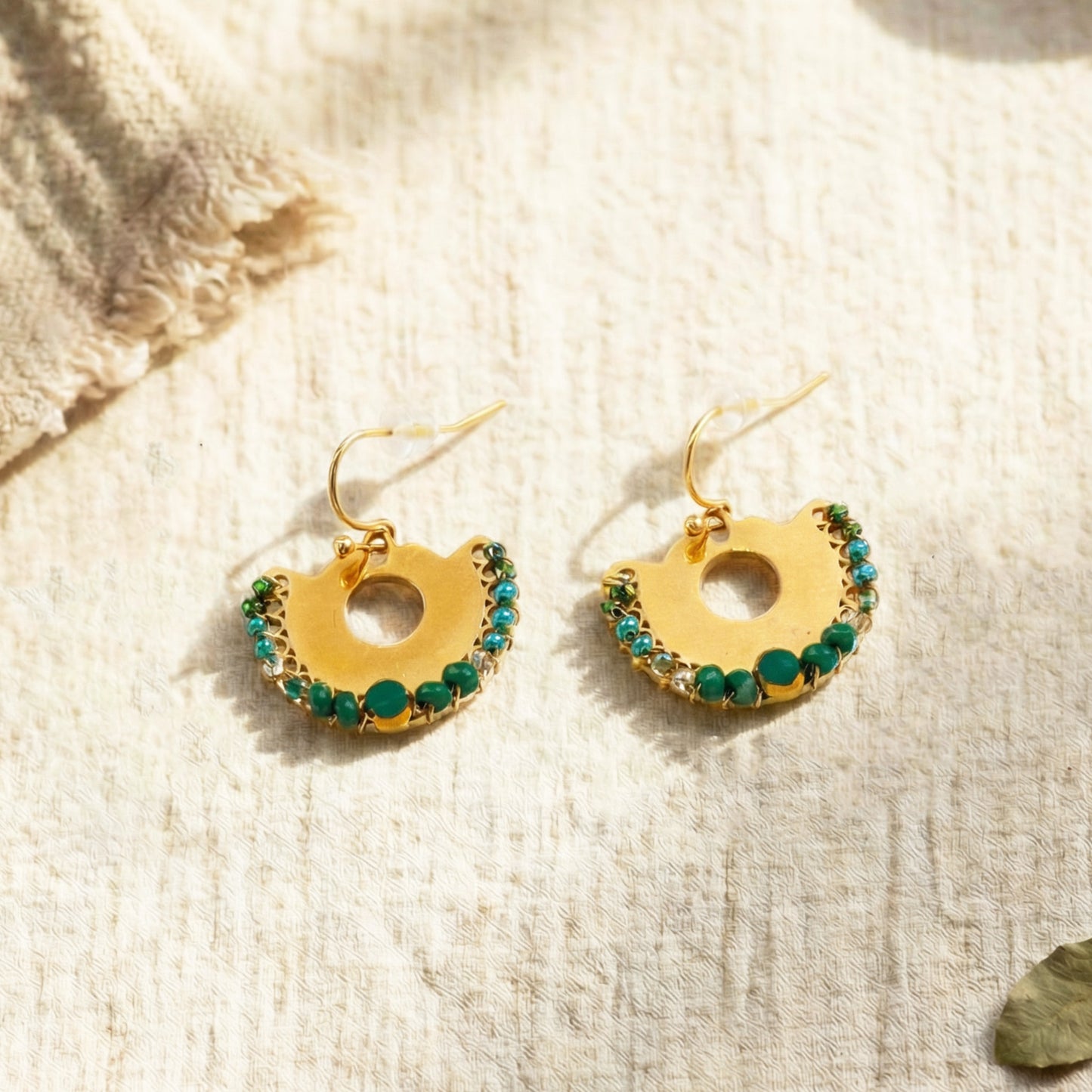 Gold earrings with green gemstones on a textured beige surface