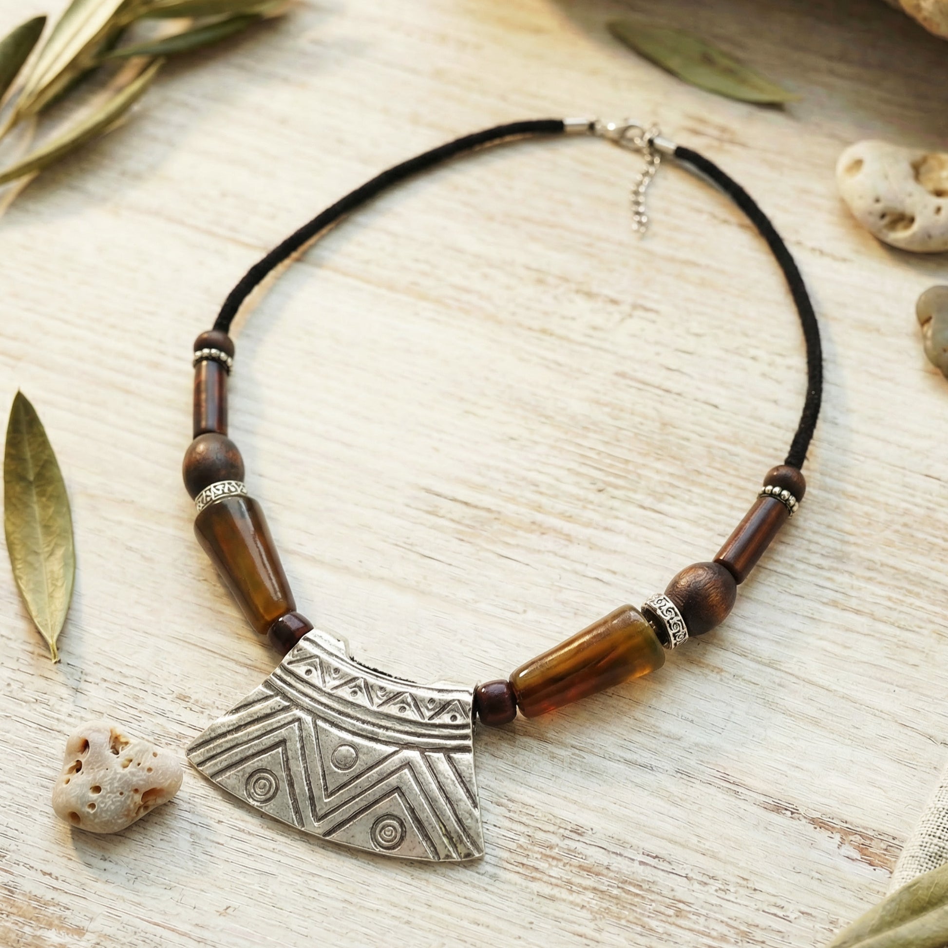 Necklace with wooden beads and a large metal pendant on a wooden surface with leaves and stones.