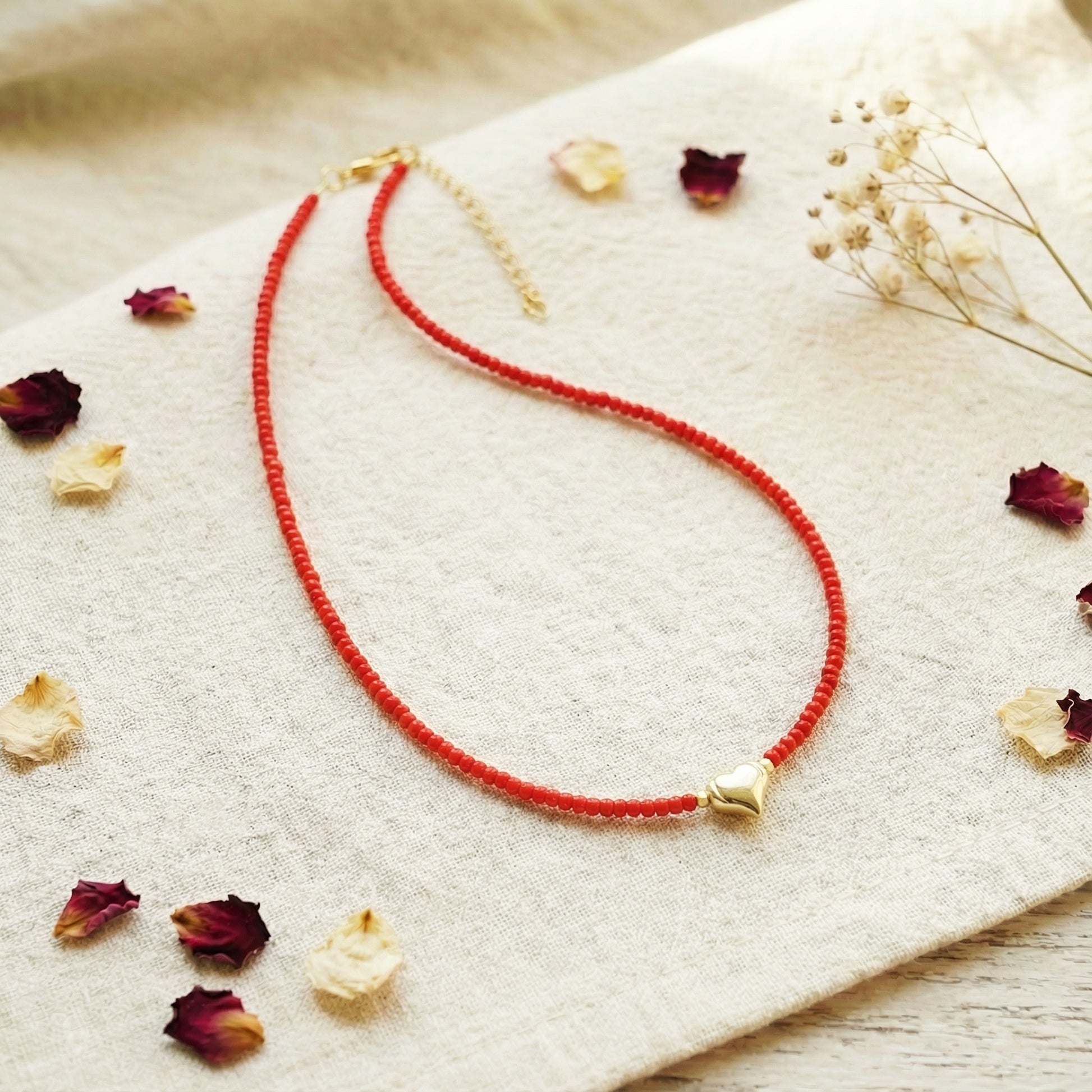 Red beaded necklace with gold accents on a light fabric background with dried flowers.