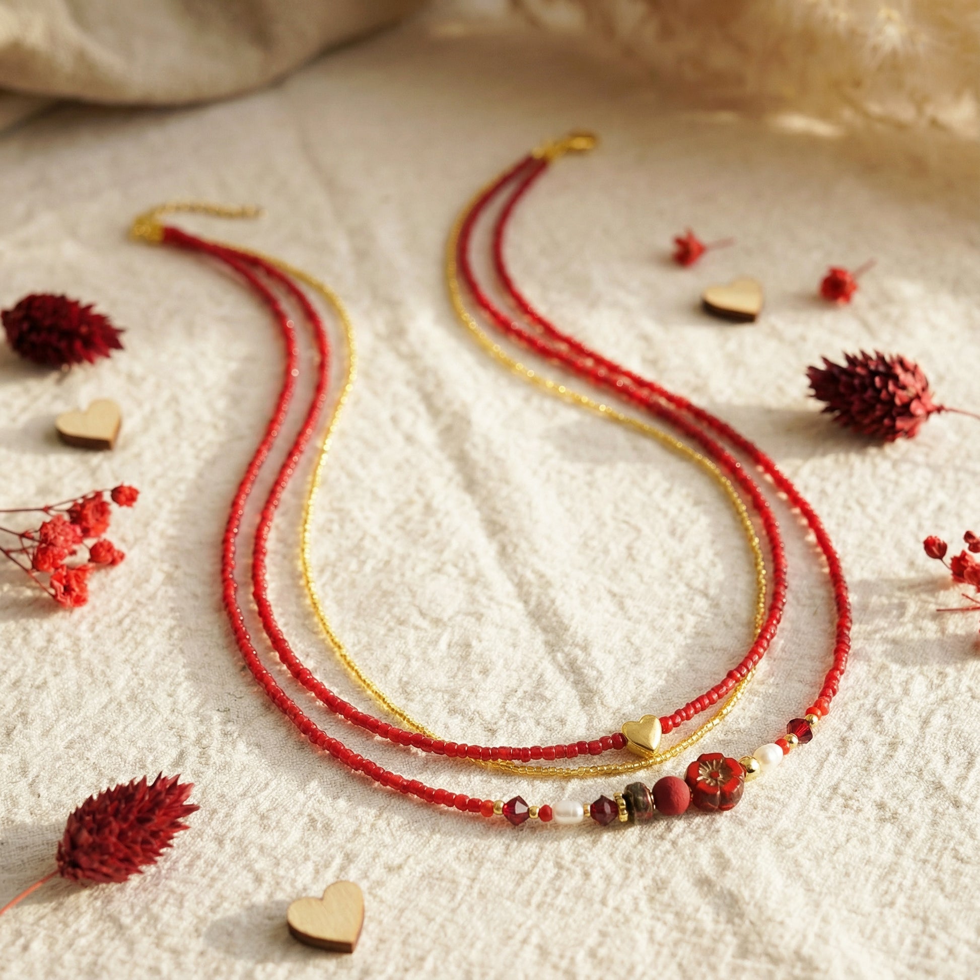 Layered beaded necklace in red, gold, and multicolor on a textured surface with dried flowers.