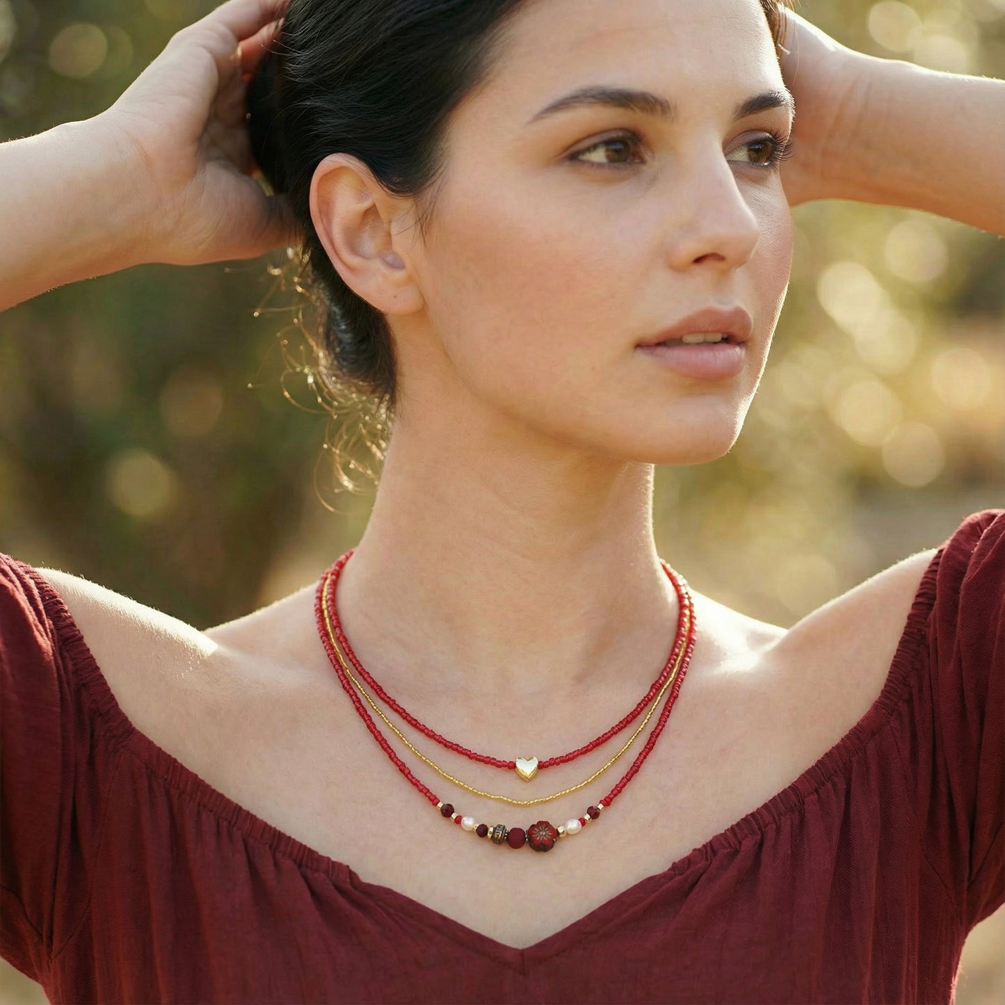 A woman wearing a red top and a layered necklace outdoors