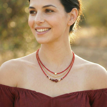 A woman wearing a red top and a layered necklace outdoors