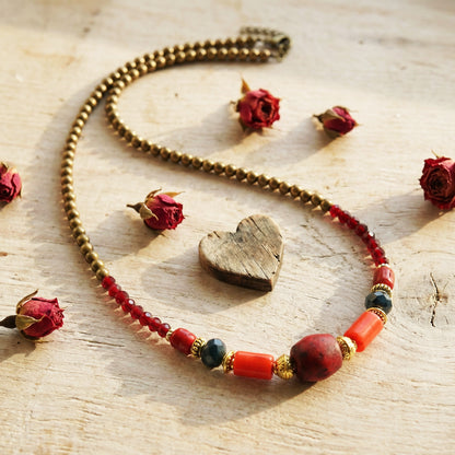 Necklace with heart-shaped pendant and red beads on a wooden surface with dried roses.