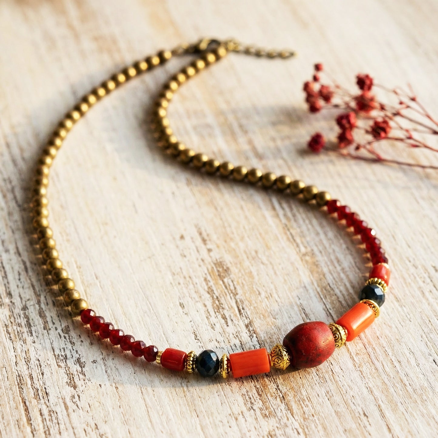 Beaded necklace with red, black, and gold beads on a wooden surface