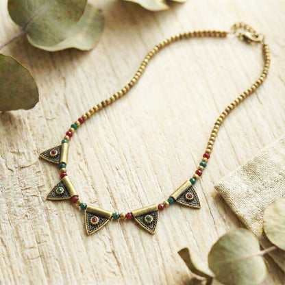 Necklace with triangle-shaped pendants on a wooden surface with leaves