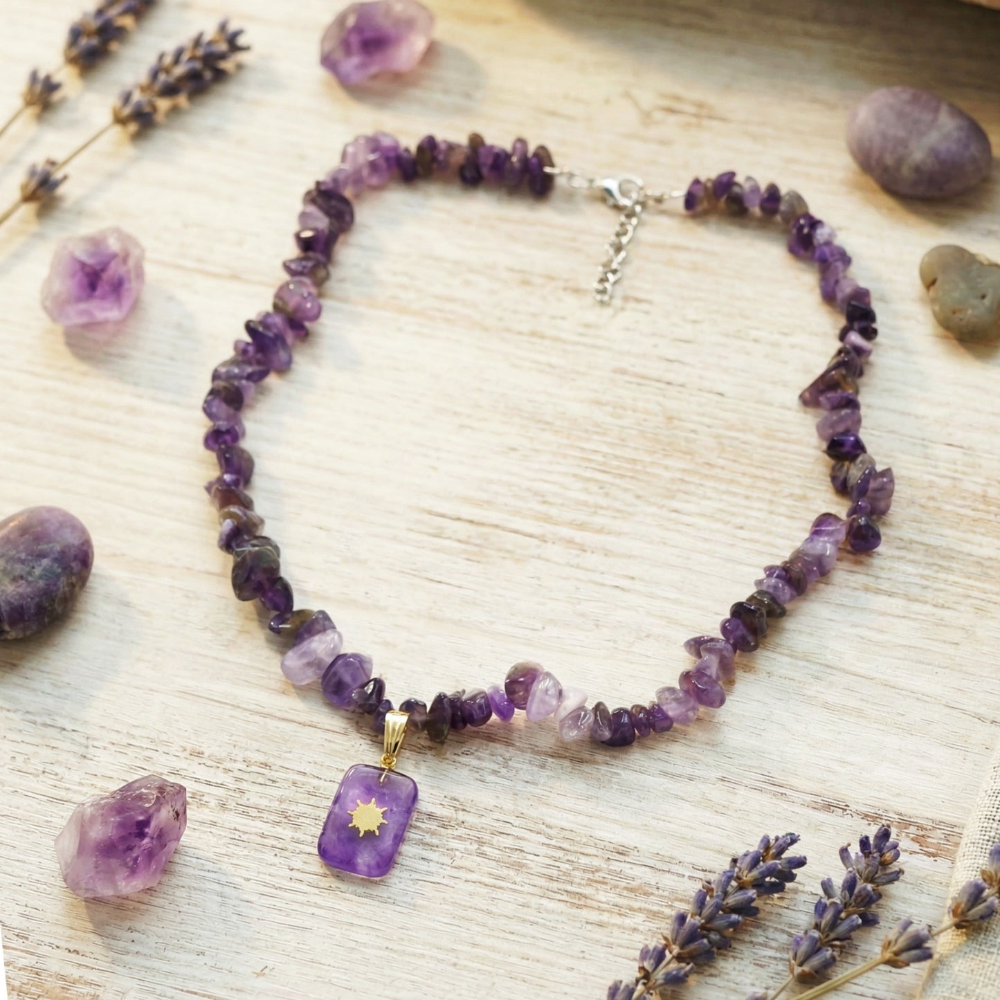 Amethyst necklace with a pendant on a wooden surface with lavender flowers and stones.