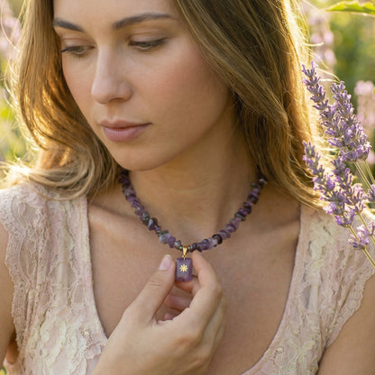 Woman wearing a purple beaded necklace with a pendant, standing in a field of lavender.