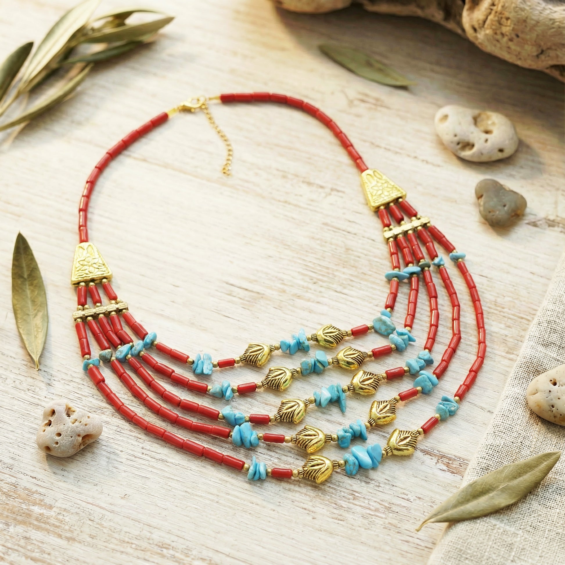 Necklace with red and gold beads on a wooden surface with leaves and stones.