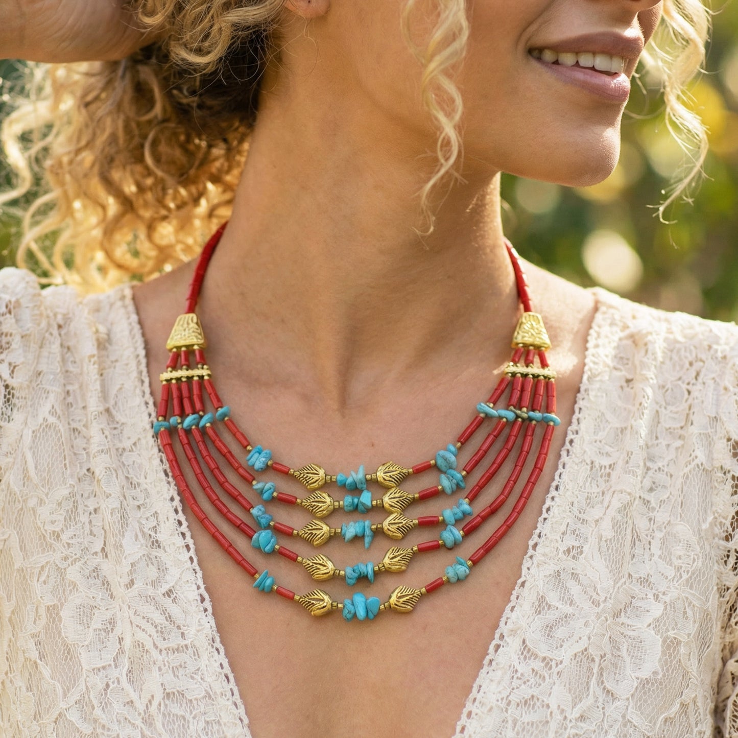 Woman wearing a red and gold beaded necklace with turquoise stones, outdoors.