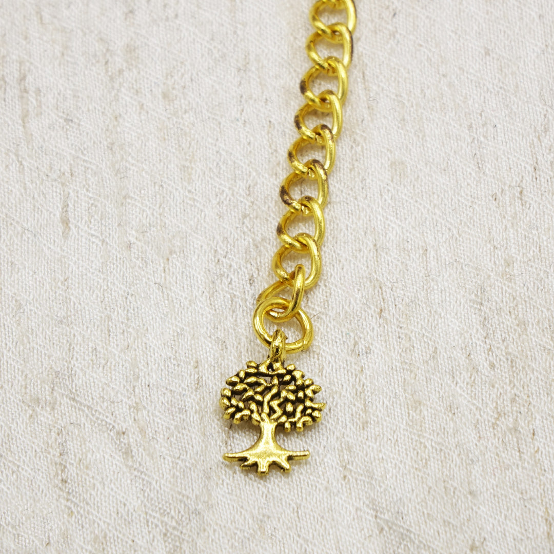 Gold chain bracelet with a tree charm on a light beige background