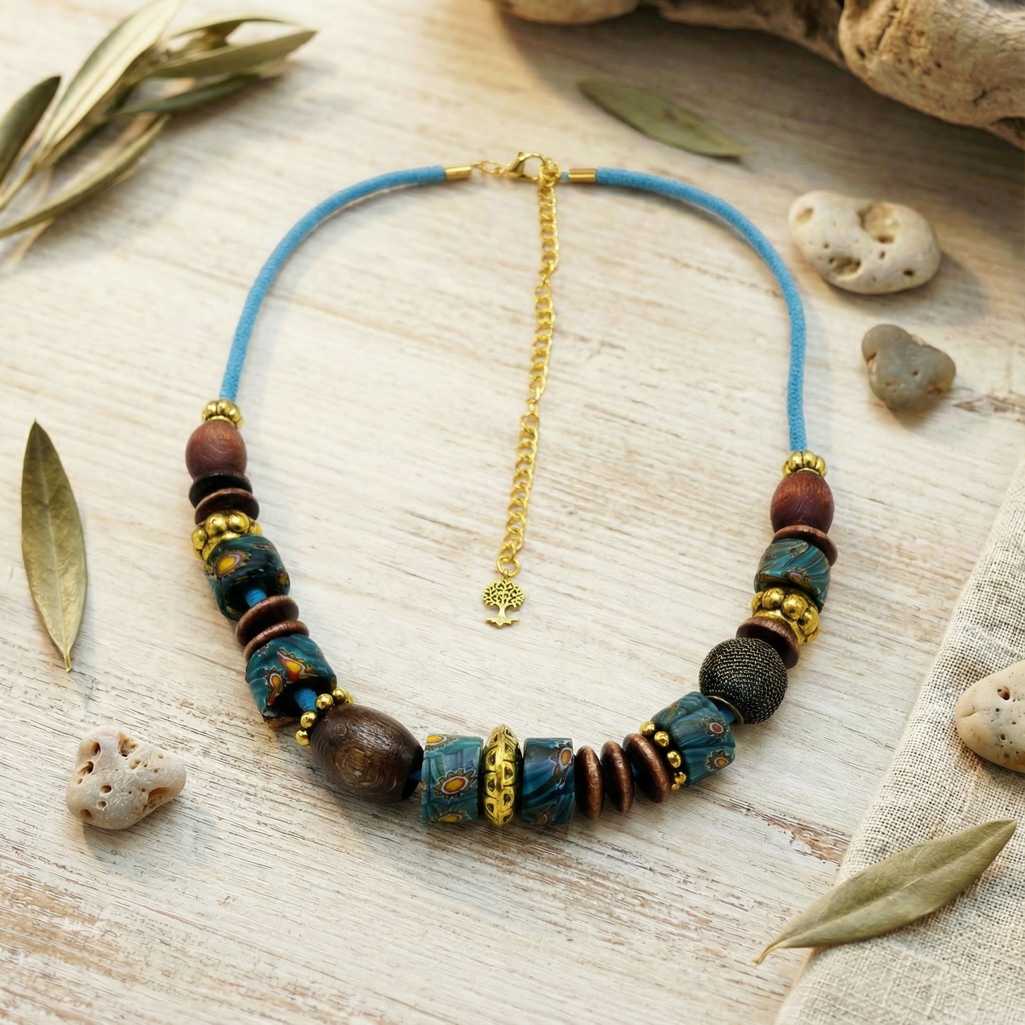 Necklace with blue cord and assorted beads on a wooden surface with leaves and stones.