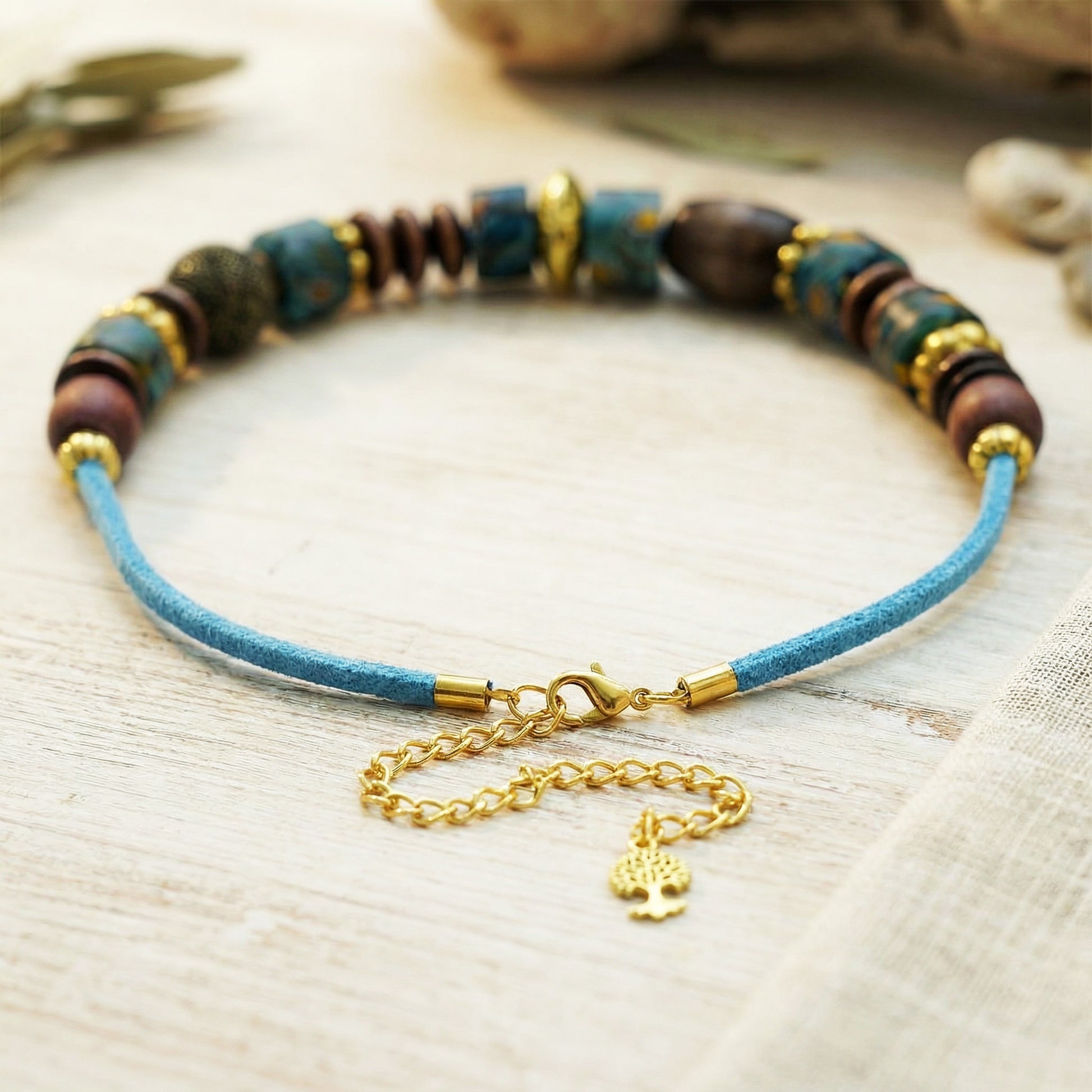 Bracelet with blue cord, multicolored beads, and gold clasp on a light wooden surface.