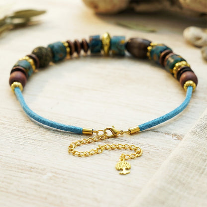 Bracelet with blue cord, multicolored beads, and gold clasp on a light wooden surface.