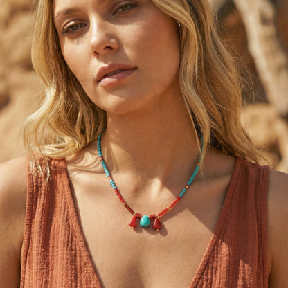 Woman wearing a necklace with turquoise and red beads against a blurred natural background