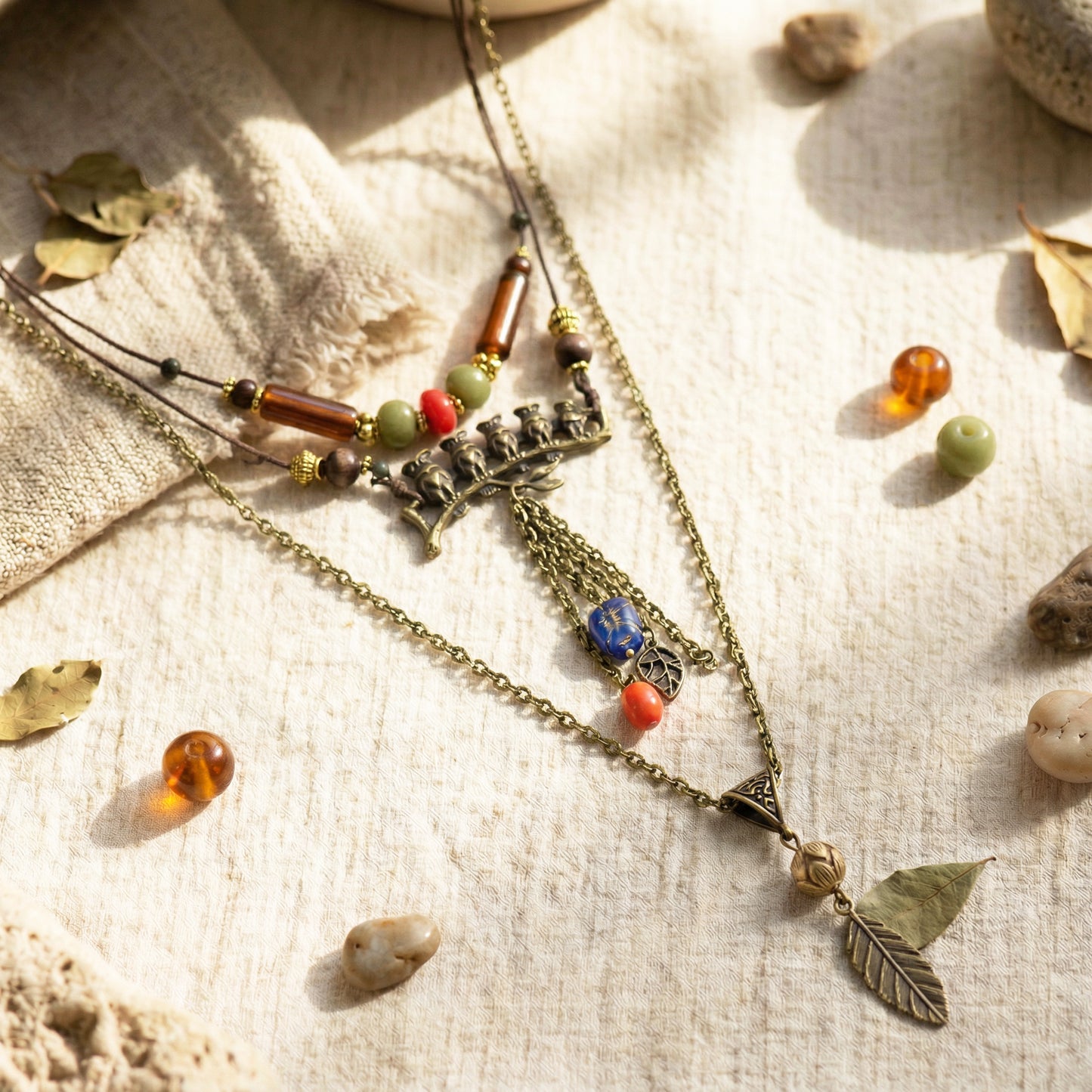 Necklace with leaf charm and beads on a textured surface with stones and leaves.